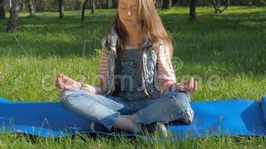 一个女孩坐在公园里做瑜伽姿势。 一个有雀斑的少女冥想。 一个穿牛仔裤的女孩在户外地毯上